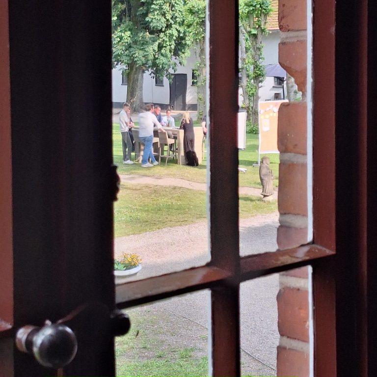 Blick durch ein geschlossenes Fenster auf ein sich beratendes Team in der Ferne